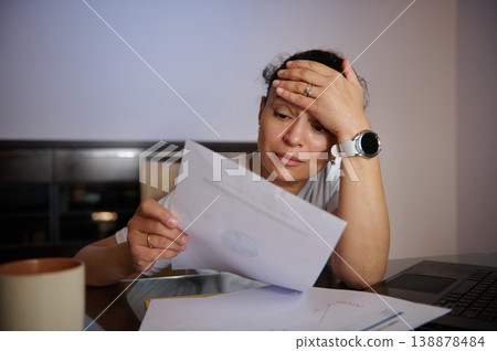 Stressed Woman Reading Bills and Financial Documents at Home With Laptop and Coffee Stressed Woman Reading Bills and Financial Documents at Home With Laptop and Coffee 138878484