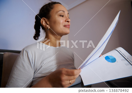 Businesswoman Reviewing Financial Report at Home Office Holding Printed Charts and Documents Businesswoman Reviewing Financial Report at Home Office Holding Printed Charts and Documents 138878492