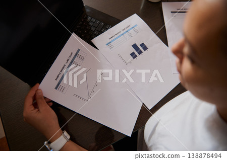 Businesswoman Reviewing Financial Charts and Invoices at Laptop Desk 138878494