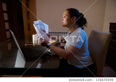 Woman Working From Home Reviewing Financial Documents At Laptop In Home Office Woman Working From Home Reviewing Financial Documents At Laptop In Home Office 138878509