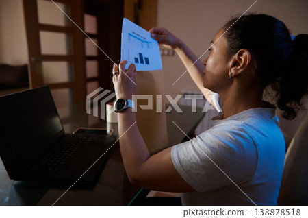 Woman Reviewing Financial Chart at Home Office Desk With Laptop and Documents Woman Reviewing Financial Chart at Home Office Desk With Laptop and Documents 138878518
