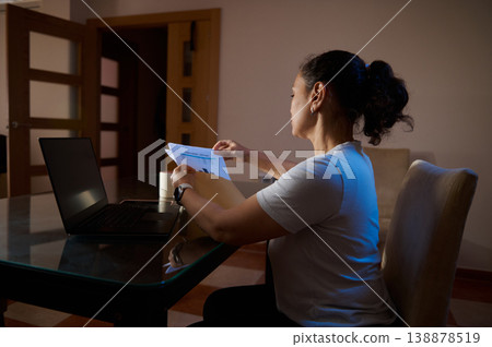 Woman Working Late at Home With Laptop and Documents in a Home Office Woman Working Late at Home With Laptop and Documents in a Home Office 138878519