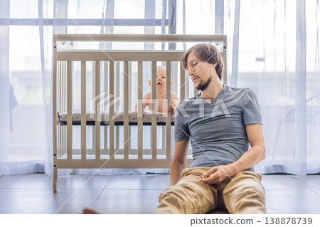 Tired father sitting by baby crib at home watching sleeping infant. Exhausted dad caring for newborn at night. Parenting fatigue, childcare responsibility, love and real family life concept 138878739