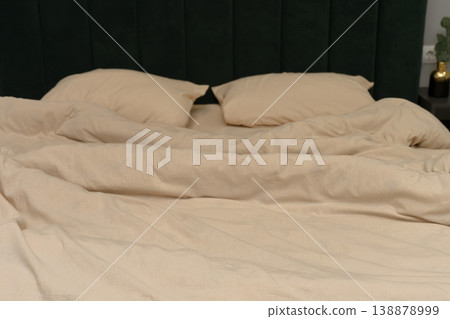 Cozy beige bedding with two pillows on a green upholstered headboard Cozy beige bedding with two pillows on a green upholstered headboard 138878999