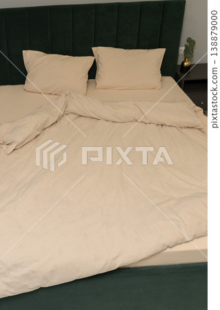 Neatly made bed with beige bedding and green upholstered headboard Neatly made bed with beige bedding and green upholstered headboard 138879000