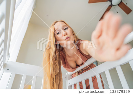Mother looking into baby crib and playing with newborn at home. Loving mom bonding with infant, smiling and interacting. Parenting care, early childhood development and emotional connection concept 138879339