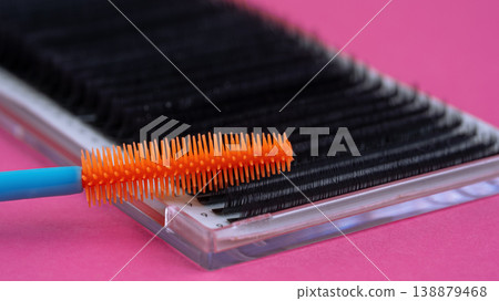 Macro close-up of an orange mascara wand on eyelash extension tray over pink background 138879468