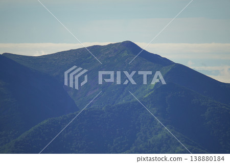 The gentle mountain ridges of Hokkaido are covered in lush green forests. The forest landscape of Hokkaido is woven together by birch and coniferous trees. 138880184