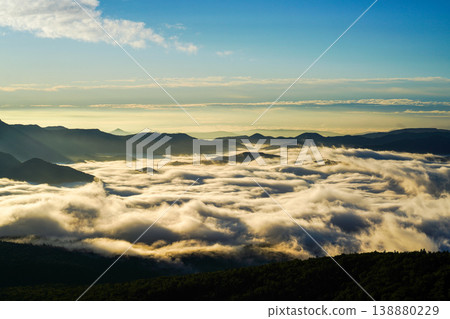 A sea of clouds against a clear blue sky at dawn, accompanied by mountain silhouettes. A fantastical morning scene with a sea of clouds spreading between the mountains. Mysterious clouds spreading between the mountains. 138880229