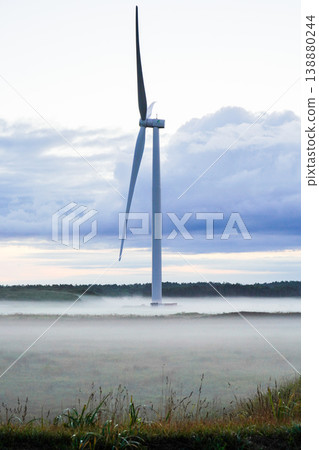 A single wind turbine stands atop a misty plain in Hokkaido. A breathtaking scene representing the magnificent nature of Hokkaido. Renewable energy: wind power. A single wind turbine stands atop a misty plain in Hokkaido. A breathtaking scene representing the magnificent nature of Hokkaido. Renewable energy: wind power. 138880244