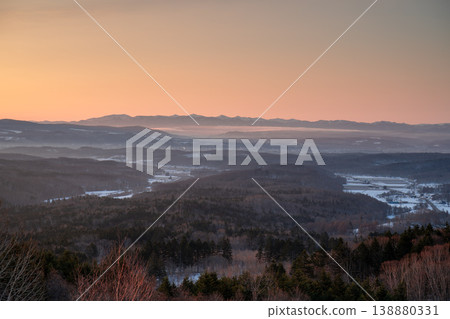 北海道冬季群山全景，粉紅夕陽映照著皚皚白雪覆蓋的山谷。這幅令人嘆為觀止的景象展現了北海道壯麗的自然風光。 138880331