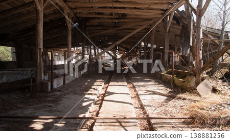 Sunlit Abandoned Barn Interior With Stalls, Wooden Beams And Dustladen Shafts Of Light Crossing Concrete Aisle 138881256