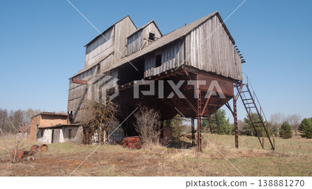 Derelict Wooden Grain Elevator On Stilts Towers Over Empty Field Under Clear Sky. Rusted Corrugated Metal Derelict Wooden Grain Elevator On Stilts Towers Over Empty Field Under Clear Sky. Rusted Corrugated Metal 138881270