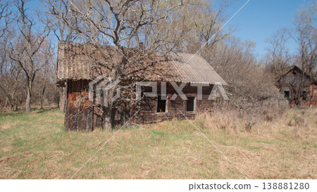 Abandoned Wooden Farmhouse In Belarus Sits Amid Overgrown Meadow Under Clear Blue Sky. Leafless Trees Press 138881280