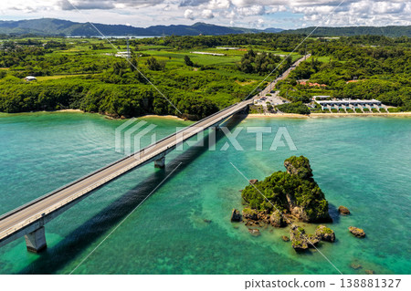 Aerial view of the emerald green sea with Kouri Bridge and small rocky reefs in Okinawa. 138881327