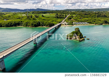 Aerial view of the emerald green sea with Kouri Bridge and small rocky reefs in Okinawa. 138881329