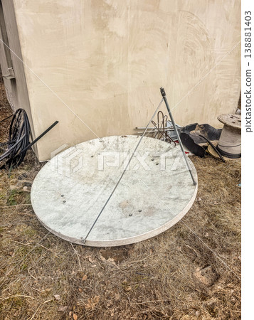 A discarded and dirty satellite dish antenna lies on the ground in a pile of junk. E-waste and obsolete technology concept.. High quality photo 138881403