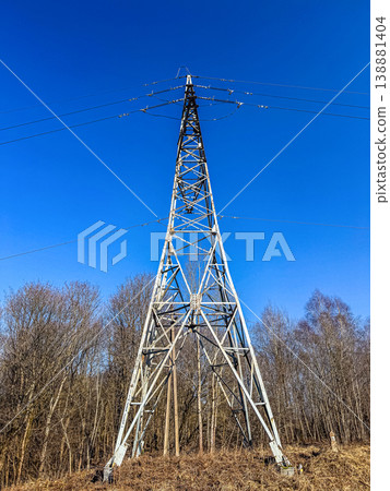 A tall metal lattice transmission tower supporting electrical power lines. Low-angle view with bare trees in the background.. High quality photo 138881404