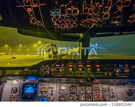 The illuminated flight deck of an airplane preparing for takeoff. A de-icing vehicle is visible on the wet tarmac through the cockpit window. High quality photo 138882040