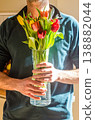 A man holding a glass vase filled with a colorful bouquet of fresh spring tulips illuminated by bright sunlight. Floral gift concept. High quality photo 138882044