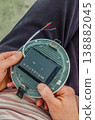 Close-up of a person's hands holding the back of a round LED panel light, showing mounting springs, driver box, and connection wires.High quality photo 138882045