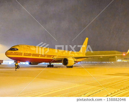 A DHL air freighter is covered in snow at the airport during a winter storm. Global shipping and delivery services continue in all weather. High quality photo 138882046