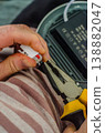 Close-up of a person's hands holding yellow pliers and a white electrical terminal connector during an LED light fixture installation.. High quality photo 138882047