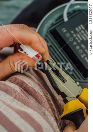 Close-up of a person's hands holding yellow pliers and a white electrical terminal connector during an LED light fixture installation.. High quality photo 138882047