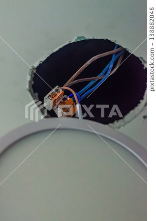 Close-up of brown and blue electrical wires joined by orange lever wire connectors in a ceiling hole during LED downlight installation.. High quality photo 138882048