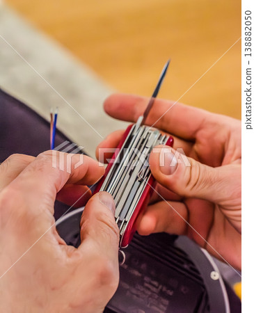 Close up of a handyman using a versatile red multitool to strip electrical wires. DIY home improvement and repair project. High quality photo 138882050