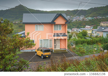 Muroran, Hokkaido, Japan - Oct 4 2024, panoramic view of a two-storey peach-colored private house with a parked off-road car at porch, with mountains on background, in cloudy weather, Muroran, Japan 138882136