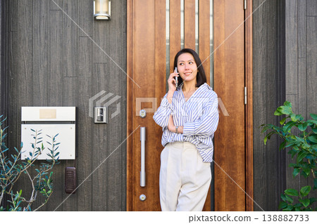 一位日本女子麵帶微笑,在獨棟房屋門口用智慧型手機通話後出門。 一位日本女子麵帶微笑,在獨棟房屋門口用智慧型手機通話後出門。 138882733