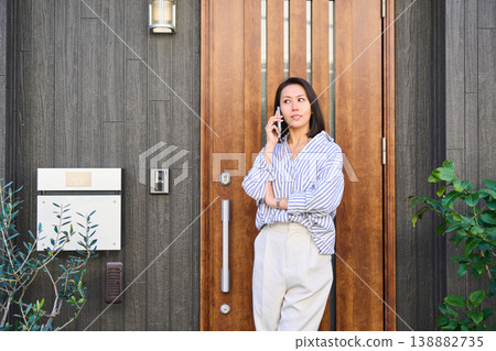 一位日本女子麵帶微笑，在獨棟房屋門口用智慧型手機通話後出門。 138882735