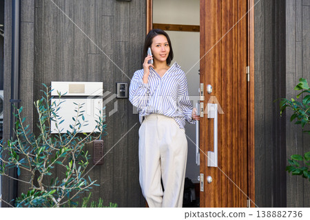 一位日本女子一邊用智慧型手機通話,一邊打開家門走了出去。 一位日本女子一邊用智慧型手機通話,一邊打開家門走了出去。 138882736