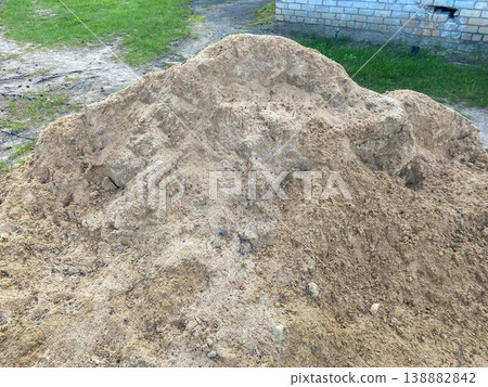 Sand pile sits on ground near building in outdoor location during daytime hours Sand pile sits on ground near building in outdoor location during daytime hours 138882842