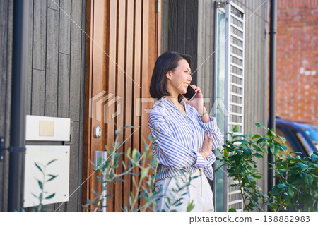 A Japanese woman's profile as she makes a phone call in front of her house. A Japanese woman's profile as she makes a phone call in front of her house. 138882983