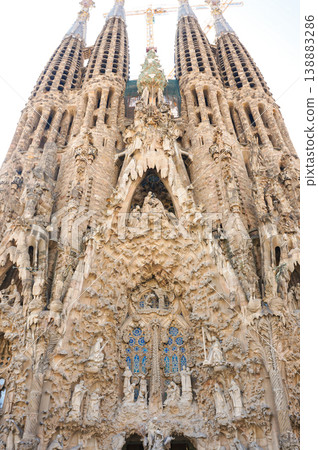 A full view of the facade of the Sagrada Familia under construction, towering against a cloudy sky. A full view of the facade of the Sagrada Familia under construction, towering against a cloudy sky. 138883286