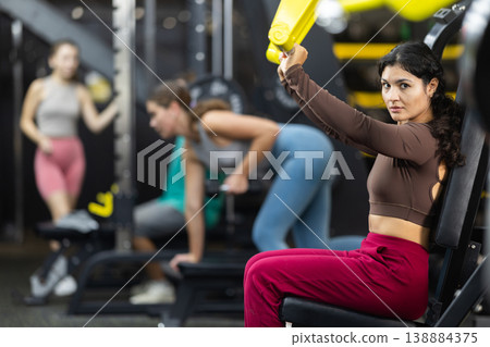 Latina woman doing shoulder press in machine Latina woman doing shoulder press in machine 138884375