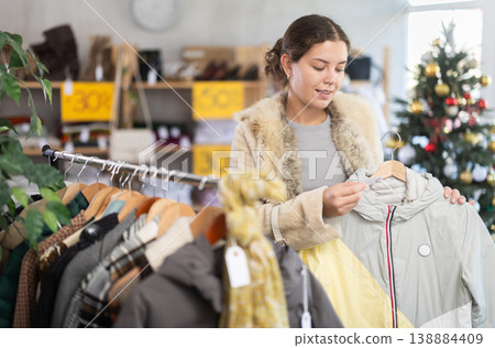 Positive young choosing down jacket in clothing store Positive young choosing down jacket in clothing store 138884409