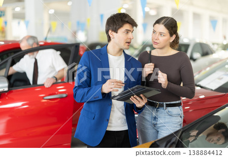 Young woman is choosing car. Car salesman helps her make right choice Young woman is choosing car. Car salesman helps her make right choice 138884412