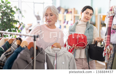 Senior female client chooses jacket, assistant consultant offers purchase bag Senior female client chooses jacket, assistant consultant offers purchase bag 138884437