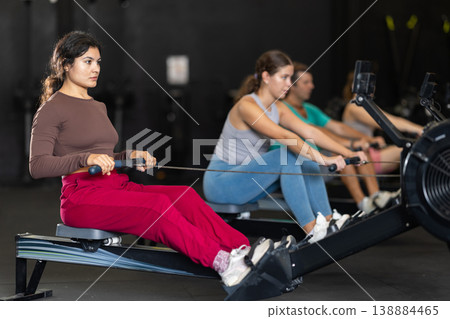 Sportive Latina girl training with rowing machine in sports hall Sportive Latina girl training with rowing machine in sports hall 138884465