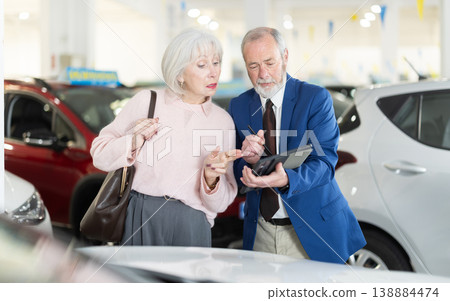 Elderly man seller showing tablet to woman in dealership Elderly man seller showing tablet to woman in dealership 138884474