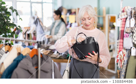 Elderly woman carefully selects fashionable handbag in clothing store Elderly woman carefully selects fashionable handbag in clothing store 138884486