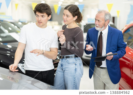 Elderly salesman selling car to young couple at dealership 138884562