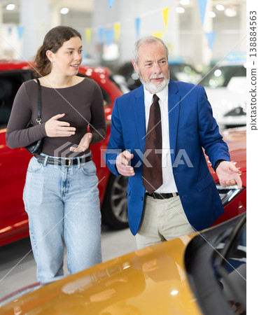 Elderly salesman selling car to young woman at dealership Elderly salesman selling car to young woman at dealership 138884563
