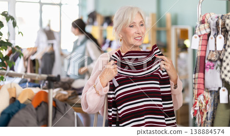 Mature woman choosing a warm knitted sweater in the store 138884574