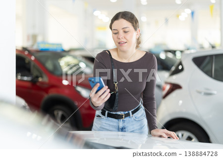 Young woman scans information about a car using a QR code at car dealership. 138884728