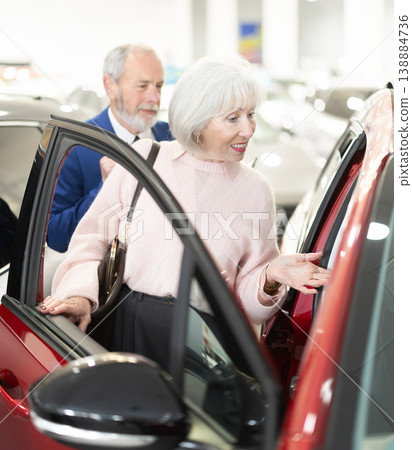 salesman shows a car to an elderly woman at a car dealership salesman shows a car to an elderly woman at a car dealership 138884736