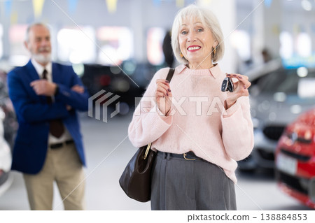 Senior salesman at car dealership offers to buy car to an elderly woman - demonstrating the best models of car dealership Senior salesman at car dealership offers to buy car to an elderly woman - demonstrating the best models of car dealership 138884853